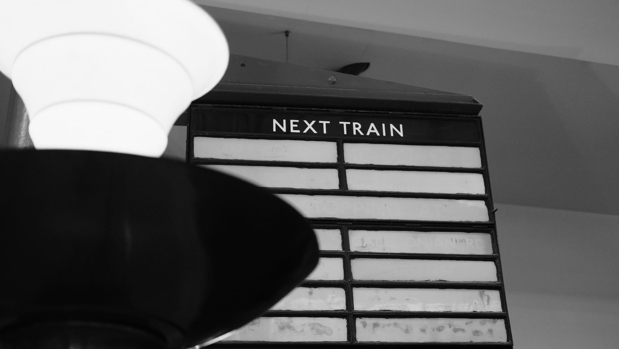 An old train timetable board on the ceiling of a train station. 